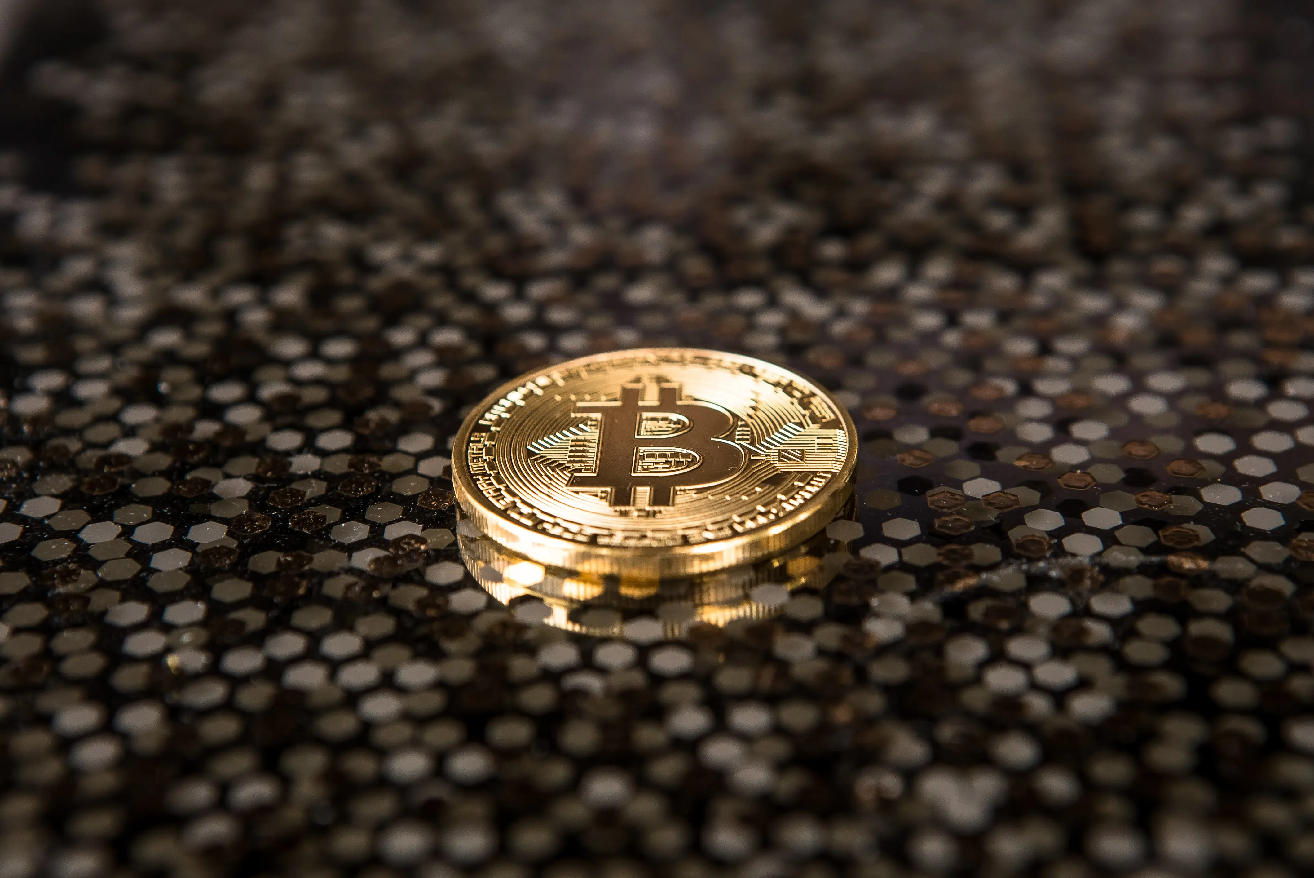 A single bitcoin on a brown and black speckled background